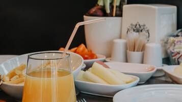 Une table avec un verre de jus d’orange, des assiettes remplies de nourriture et un vase de fleurs violettes.