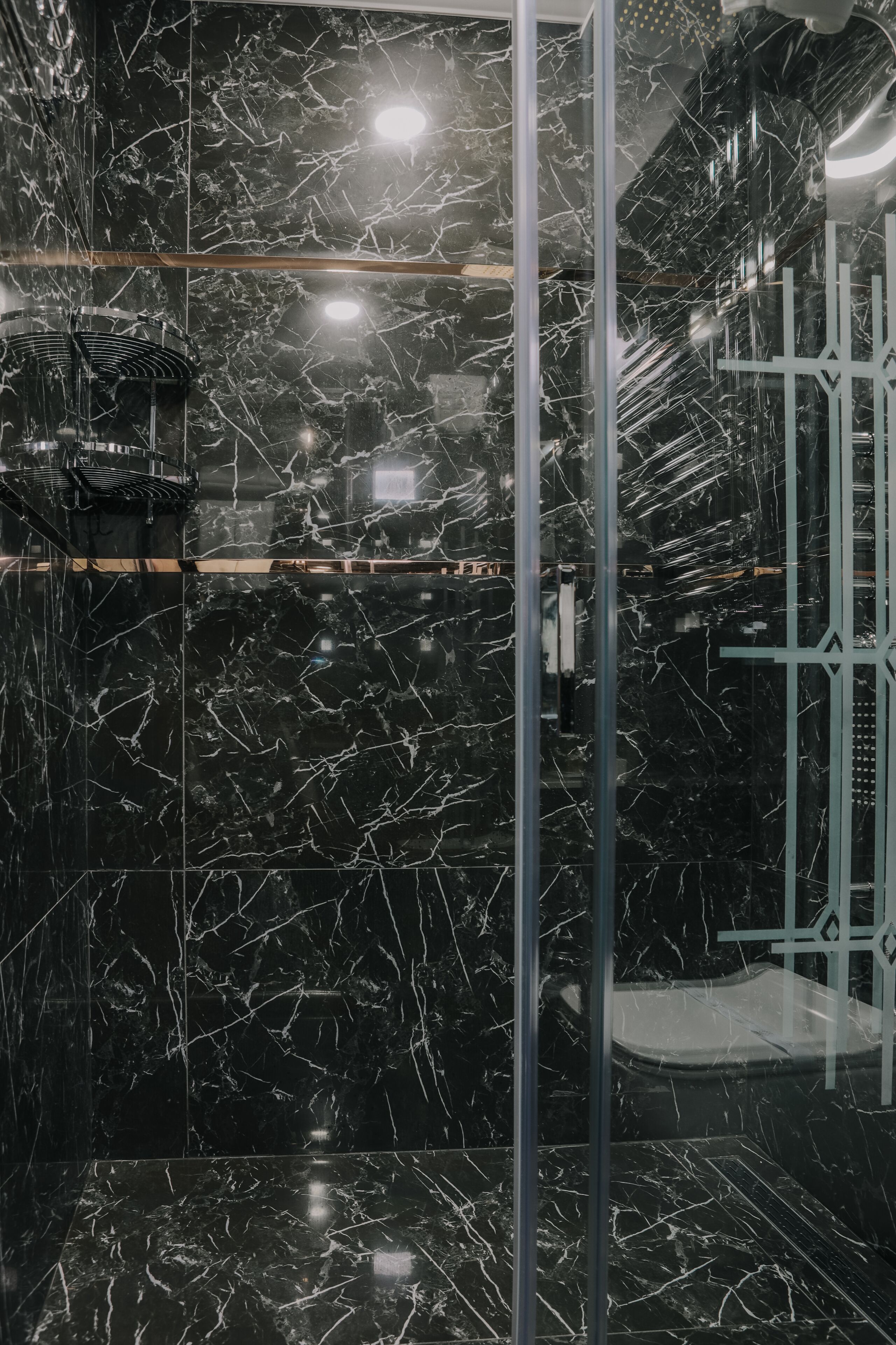 Un baño moderno con azulejos de mármol negro y mampara de cristal.