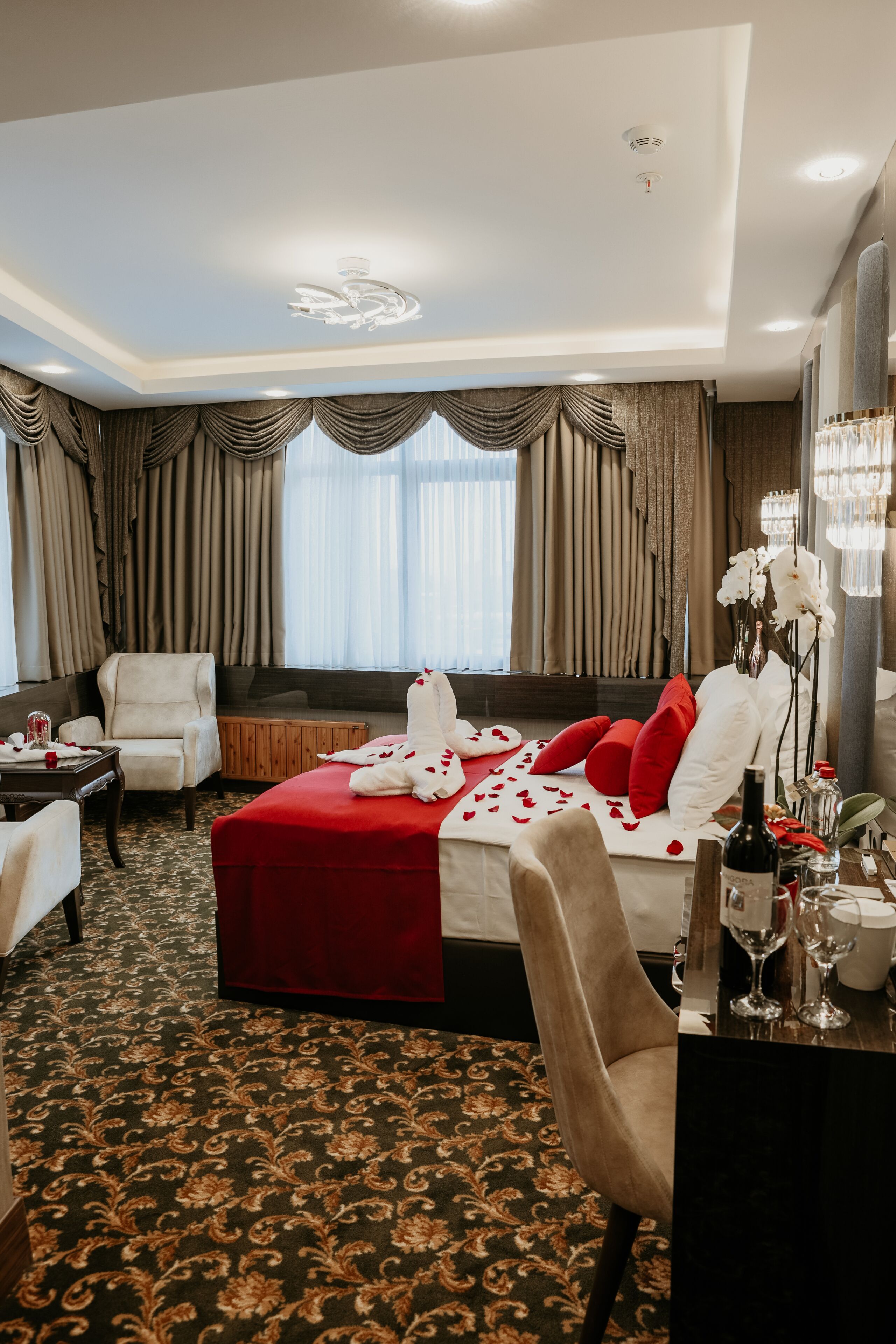 Une chambre d’hôtel avec un lit, un canapé, une chaise, une table avec une bouteille et un vase de fleurs.