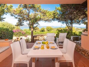 Una terrazza con tavolo apparecchiato per due, circondata da sedie in vimini bianco, con vista panoramica sul mare e sul verde.