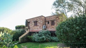 Een stenen huis met een rode pannendak, omgeven door weelderige begroeiing en een omheinde tuin.