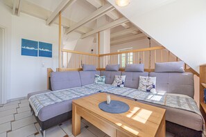 Una habitación moderna y bien iluminada con un amplio sofá, una mesa de centro de madera y una escalera que lleva a un nivel superior.
