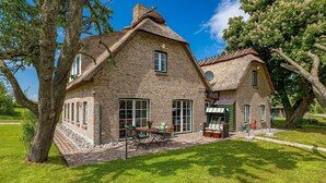 A two-story brick house with a thatched roof, large windows, and a paved patio with outdoor furniture.