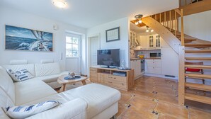 A modern living room with a sofa, TV, and artwork. A staircase leads to a kitchen and dining area.
