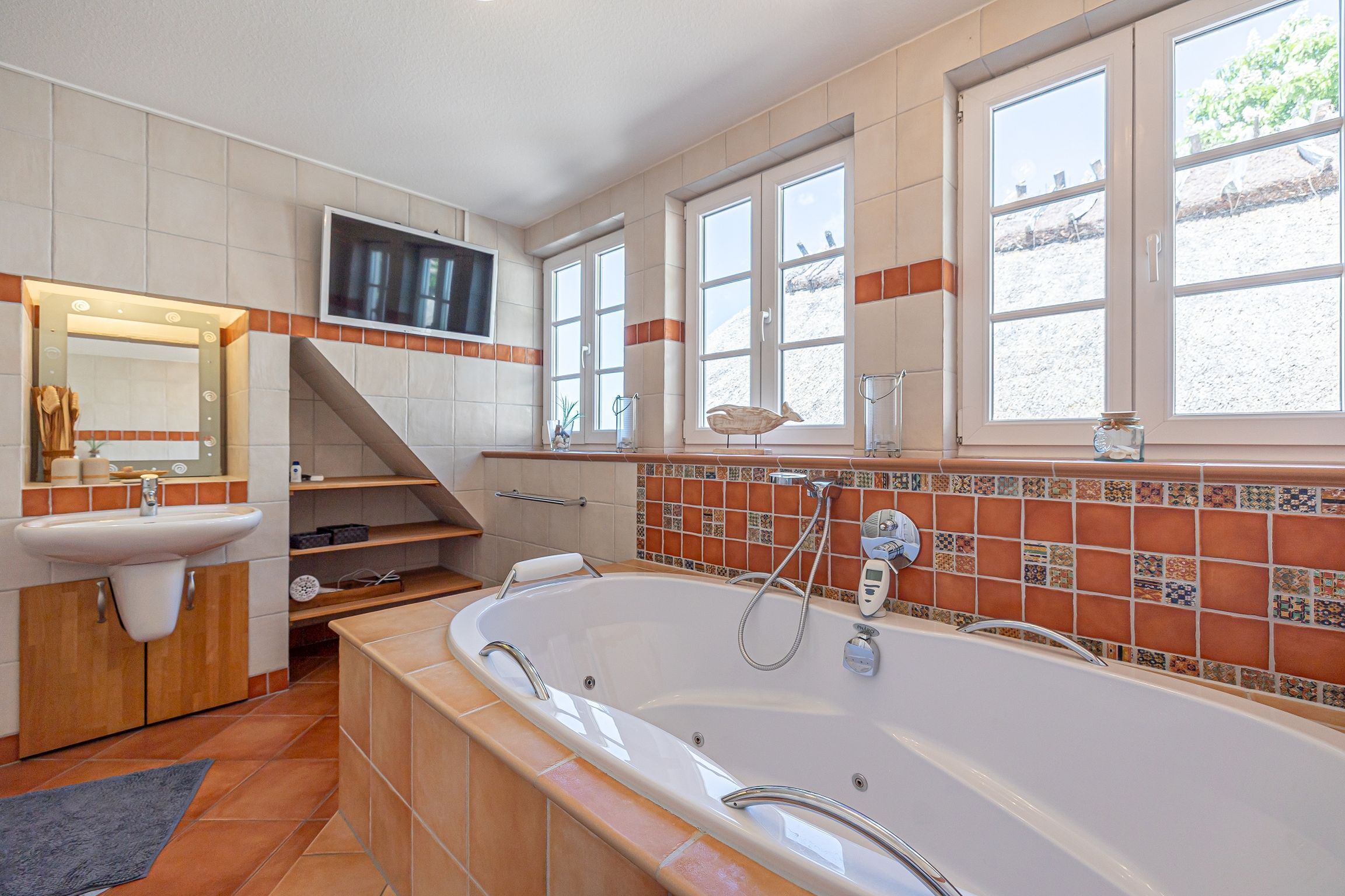 A bathroom with a large bathtub, a sink, a mirror, and a TV mounted on the wall.