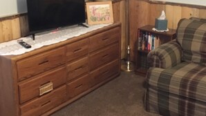 A living room with a wooden cabinet, a television, a lamp, a small Christmas tree, and a plaid sofa. - Rustic Hideaway -pets welcome, downtown- (Idaho Falls)