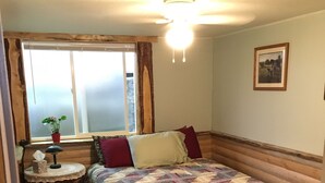 A cozy room with a bed, a small table with a lamp, a window with curtains, and a ceiling light. - Rustic Hideaway -pets welcome, downtown- (Idaho Falls)