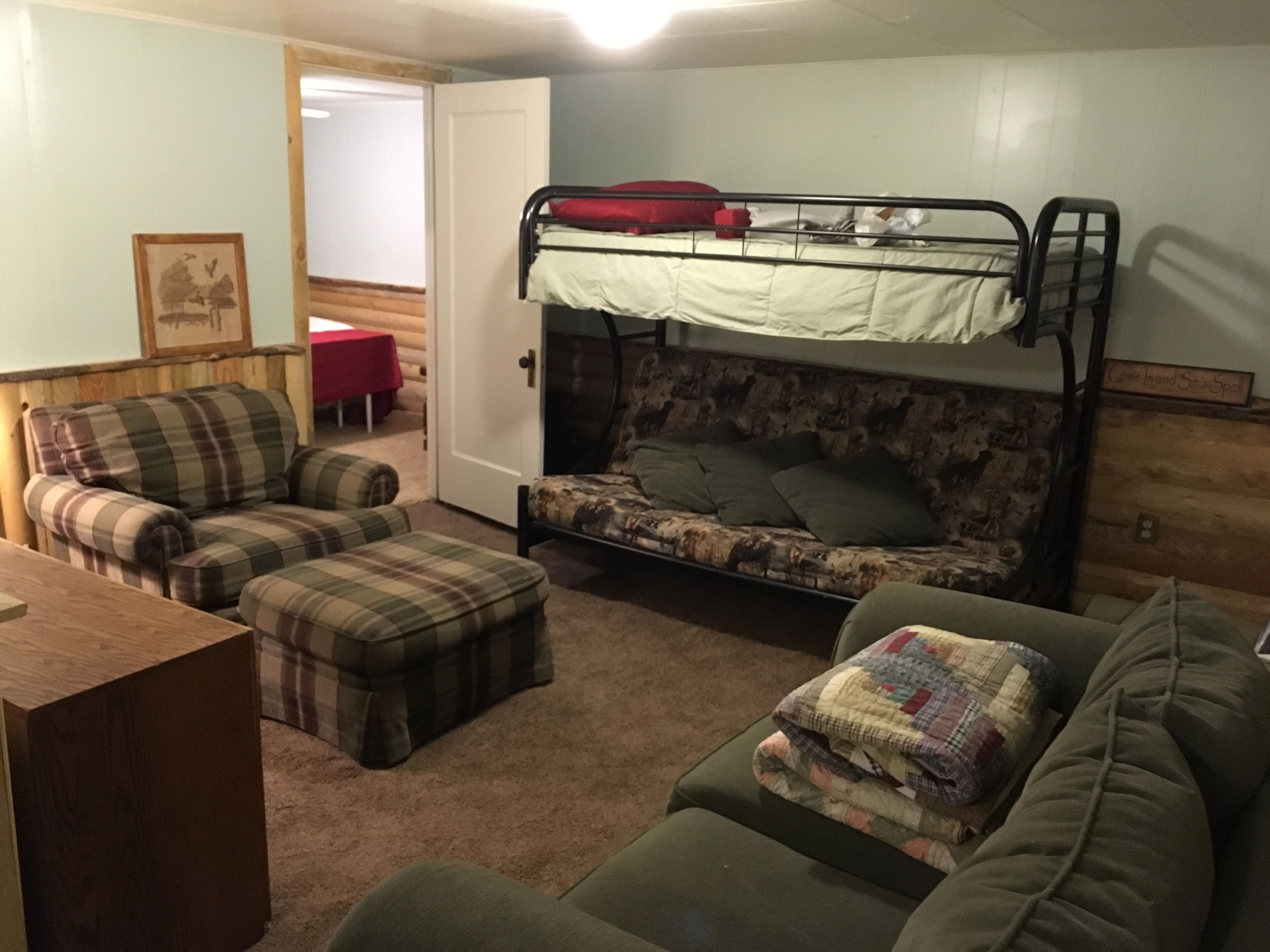 A cozy room with a bunk bed, a plaid sofa, a green couch, and a wooden table.