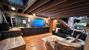 A cozy living room with a wooden floor, a leather sofa, a TV, and a bar area with a wooden ceiling. - The Cotter Fish and Game (Cotter)