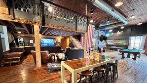 A spacious indoor area with wooden floors, a pool table, a bar area with stools, and a staircase leading to an upper level. - The Cotter Fish and Game (Cotter)