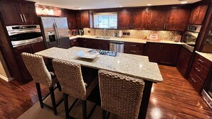 A modern kitchen with dark wood cabinets, stainless steel appliances, a granite countertop, and a central island with bar stools. - The Cotter Fish and Game (Cotter)