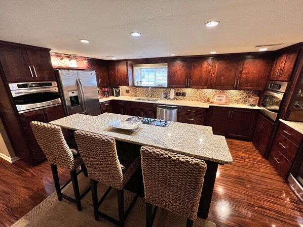 A modern kitchen with dark wood cabinets, stainless steel appliances, a granite countertop, and a central island with bar stools. - The Cotter Fish and Game (Cotter)