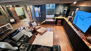A modern living room with a black leather sofa, a wooden floor, and a large flat-screen TV displaying a map. - The Cotter Fish and Game (Cotter)