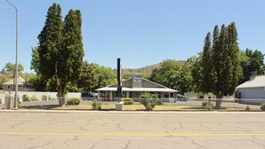 A motel with a single-story structure, a fenced parking area, and a hill in the background. - Budget Inn Yreka (Yreka)