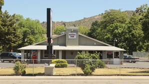 A small, single-story Budget Inn with a simple, functional design, located in a semi-rural area with trees and hills in the background. - Budget Inn Yreka (Yreka)