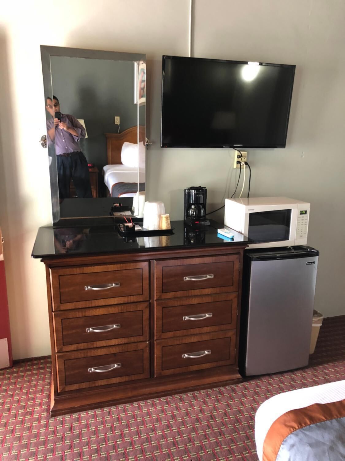 Habitación de hotel con cómoda de madera, televisor de pantalla plana, cafetera, microondas y refrigerador.