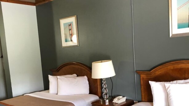 A hotel room with two beds, wooden headboards, a nightstand with a lamp, and a framed picture on the wall. - Budget Inn Yreka (Yreka)