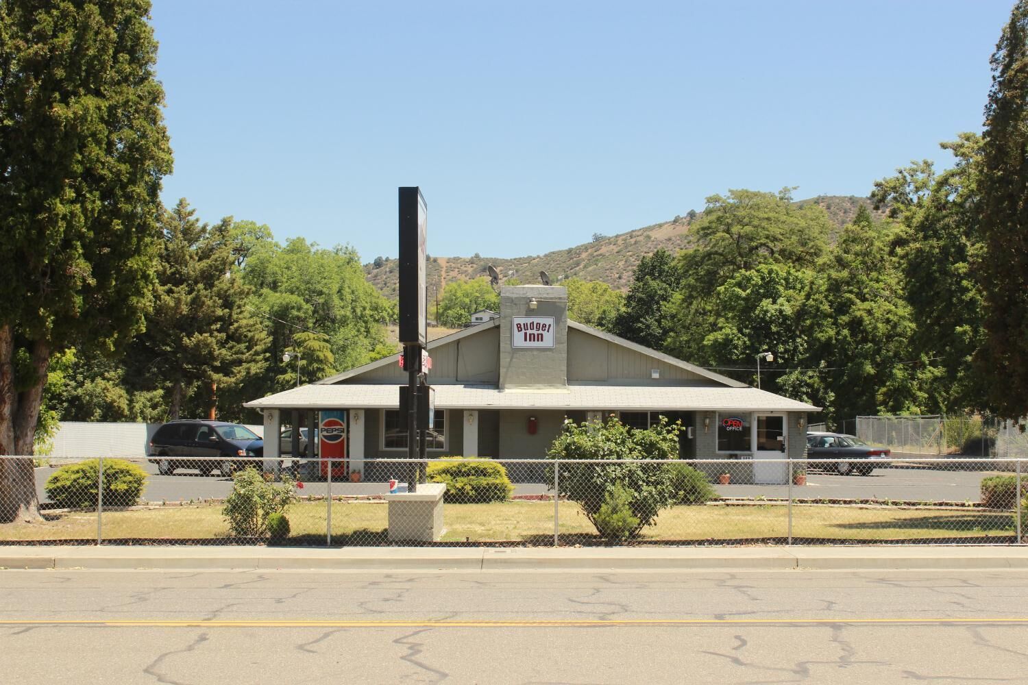 A single-story motel with a flat roof, a signboard, and a fenced parking area.