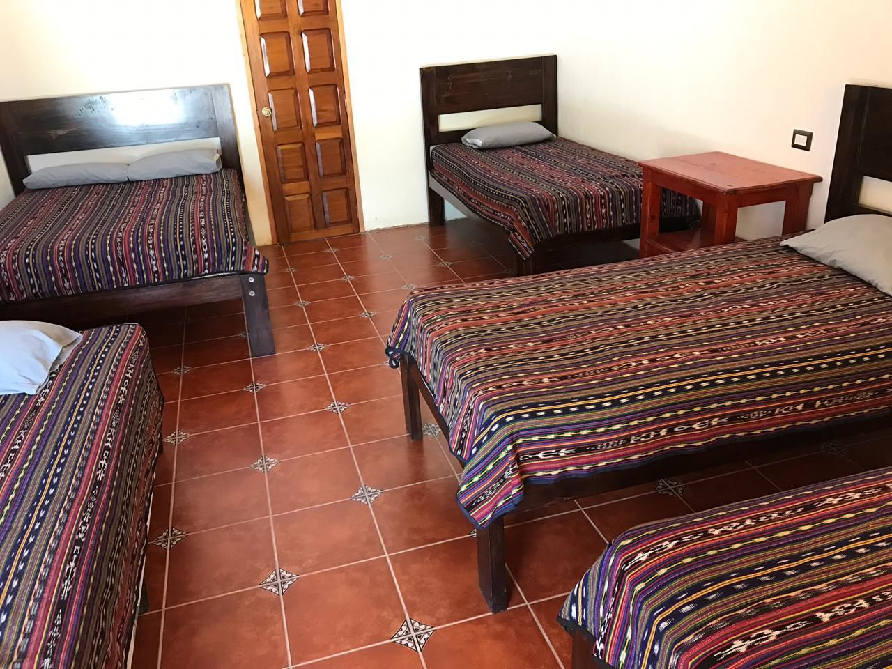 A room with four beds, each with patterned bedding, a wooden door, and a tiled floor.