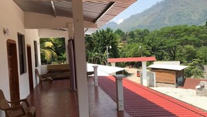 A covered outdoor area with a red roof, wooden benches, and a view of a mountainous landscape. - Lauris Hotel (San Agustin Lanquin)