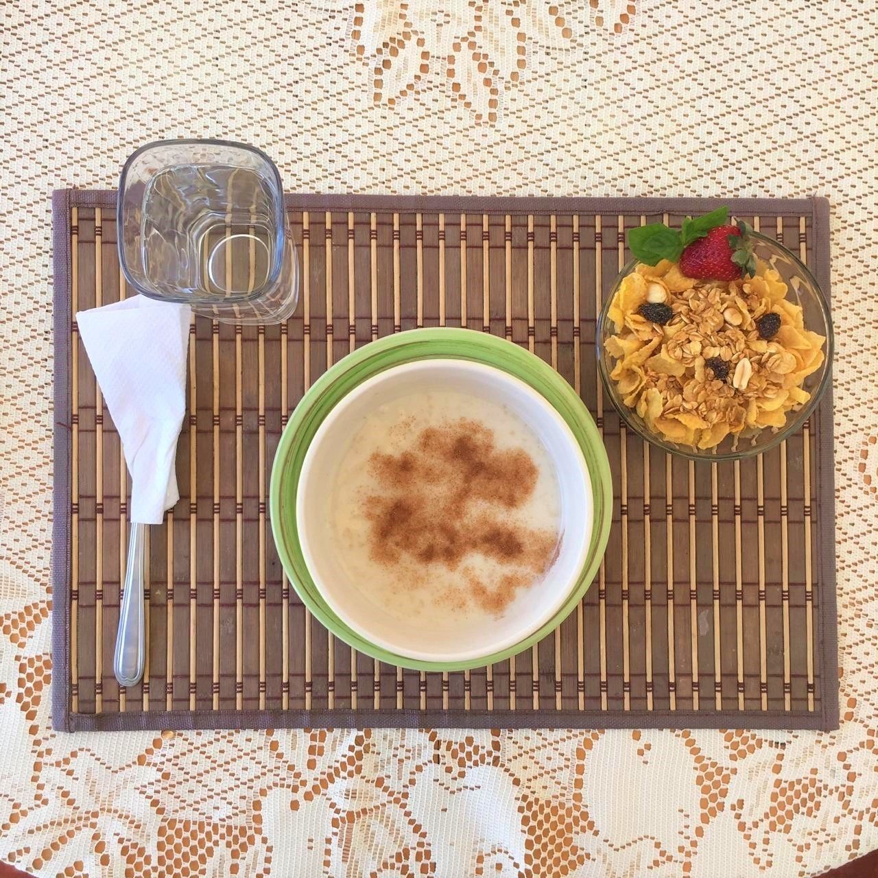 Un desayuno con un tazón de avena, un vaso de agua y un tazón de granola con frutas, todo sobre un mantel tejido.