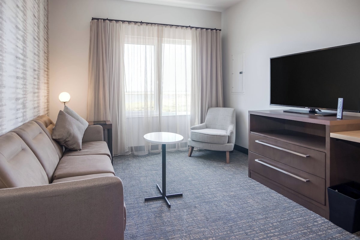 A hotel room with a sofa, armchair, small round table, TV, and a cabinet.