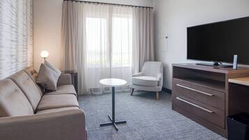 A hotel room with a sofa, armchair, small round table, TV, and a cabinet.