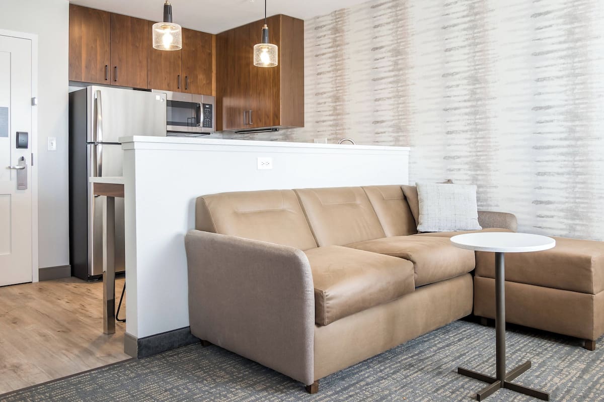 A modern kitchen with wooden cabinets, stainless steel appliances, and a beige sectional sofa.