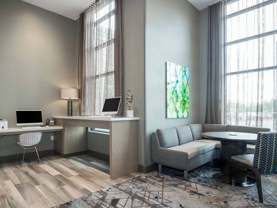 A hotel room with a desk, computer, chair, sofa, and a dining table with chairs.