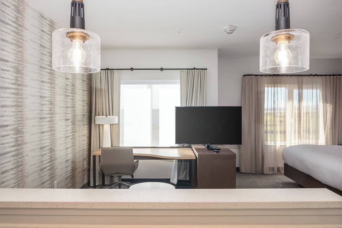 A hotel room with a bed, desk, chair, TV, and two pendant lights.