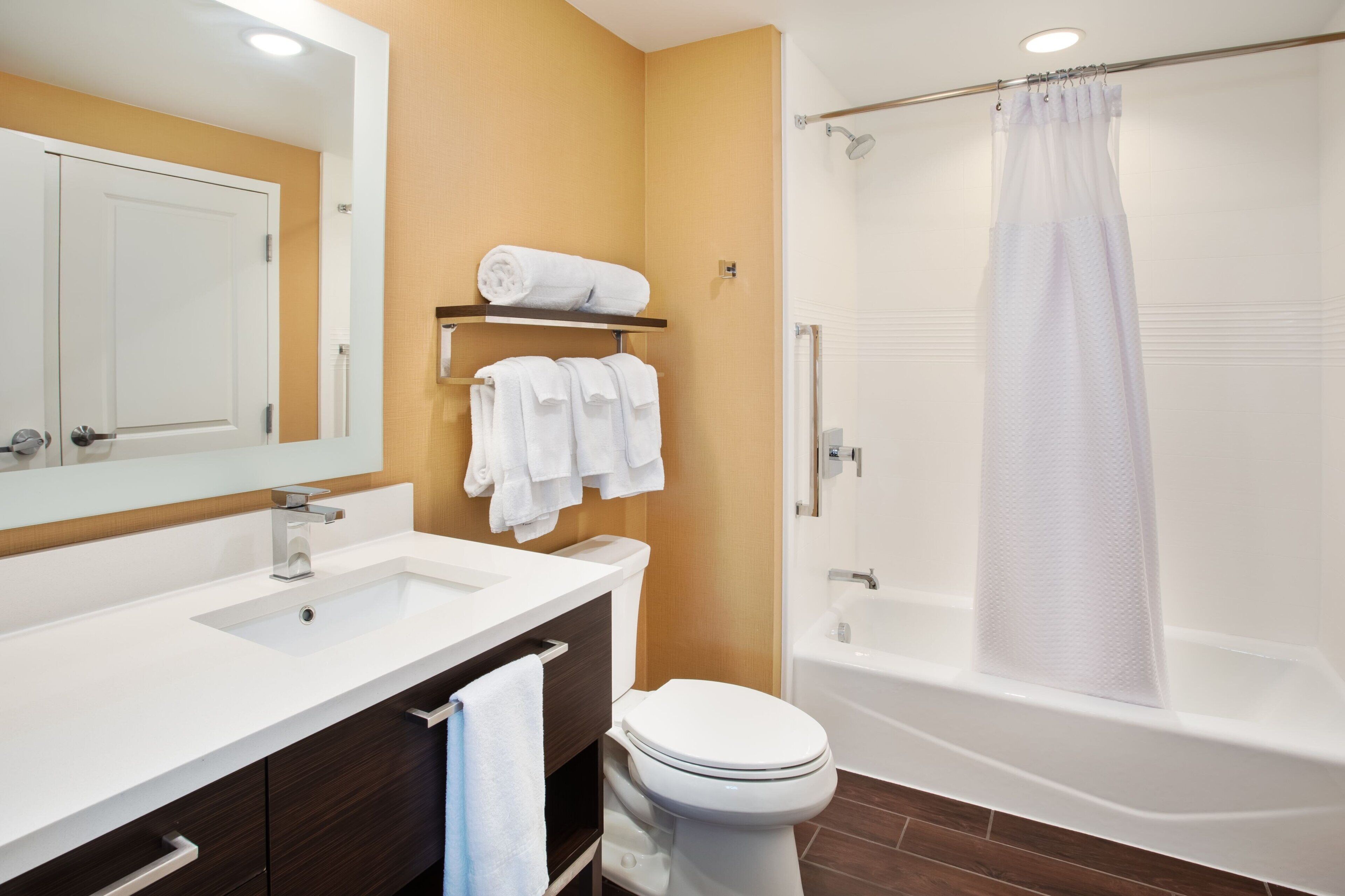 Une salle de bain avec un lavabo blanc, des toilettes, une douche avec un rideau et un miroir au-dessus du lavabo.