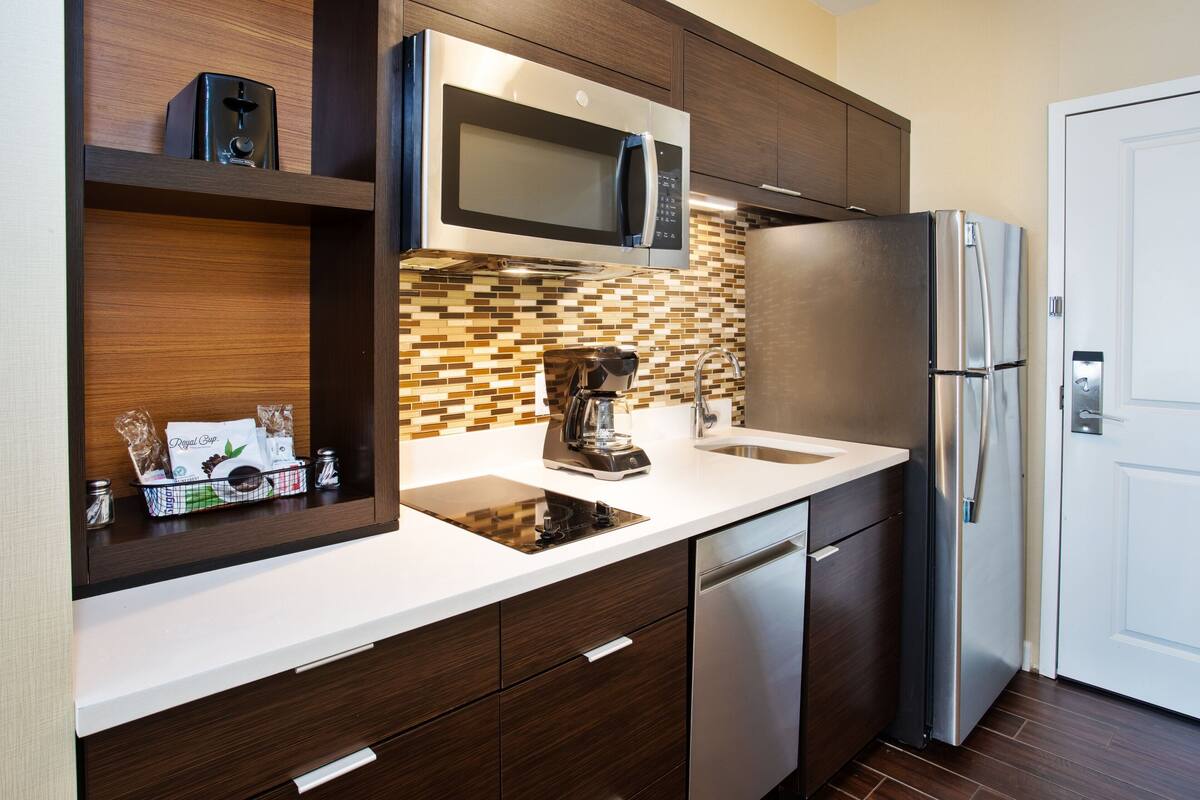 A modern kitchen with a built-in microwave, stainless steel refrigerator, and a coffee maker on the counter.