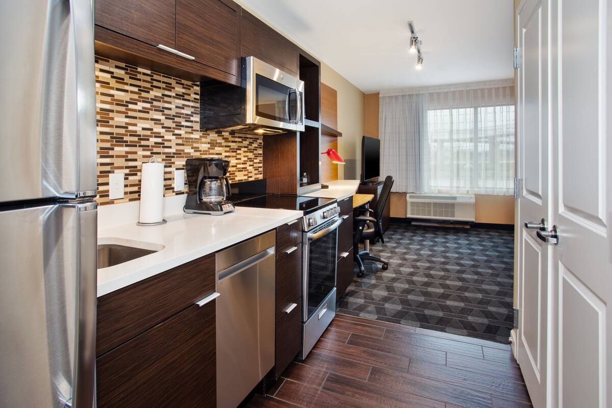 A modern kitchen with stainless steel appliances, a microwave, and a built-in oven. There is a dining area with a table and chairs, and a large window providing natural light.
