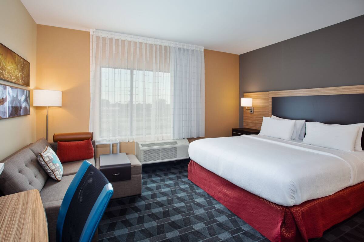 A hotel room with a bed, a sofa, a desk, and a window with curtains.