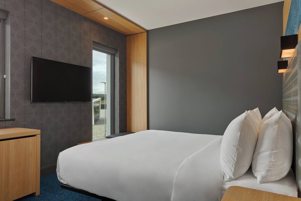 Ein modernes Hotelzimmer mit einem großen Bett, einem flachbildfernseher an der Wand und einem Holztisch.