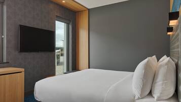 Una habitación de hotel moderna con una cama grande, un televisor de pantalla plana montado en la pared y un escritorio de madera.