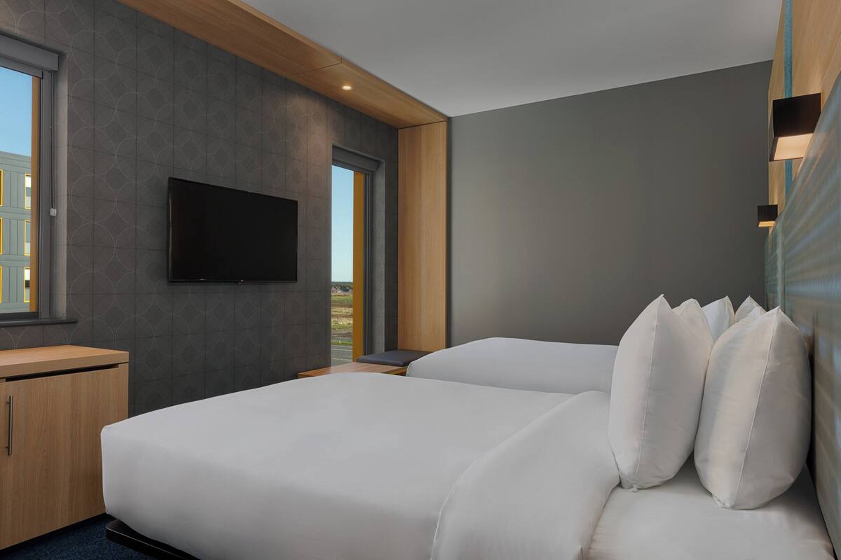 Ein modernes Hotelzimmer mit einem großen Bett, einem an der Wand befestigten Flachbildfernseher und einem Nachttisch aus Holz.