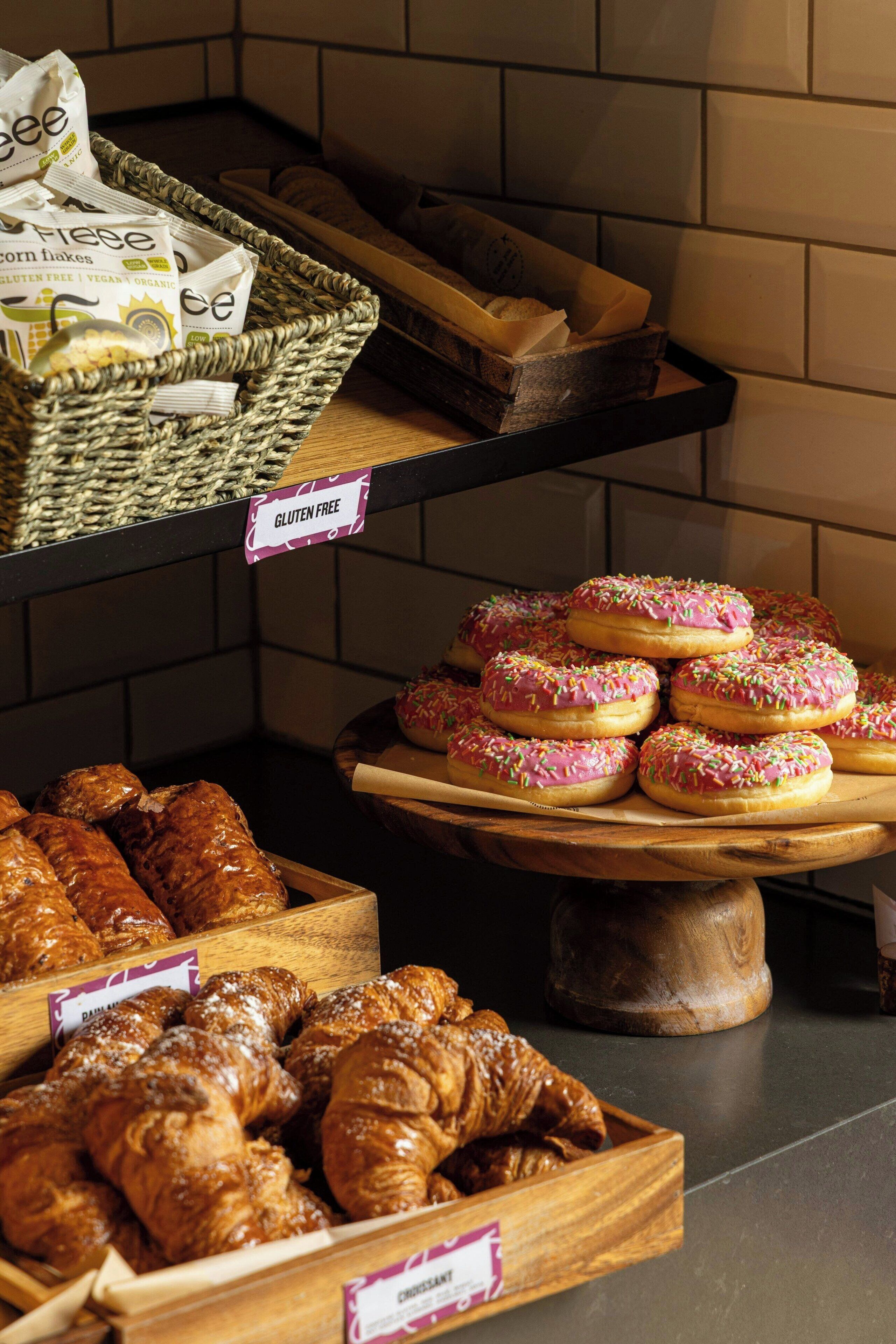 Mostrador de panadería con opciones sin gluten y veganas, que incluye pasteles y rosquillas.