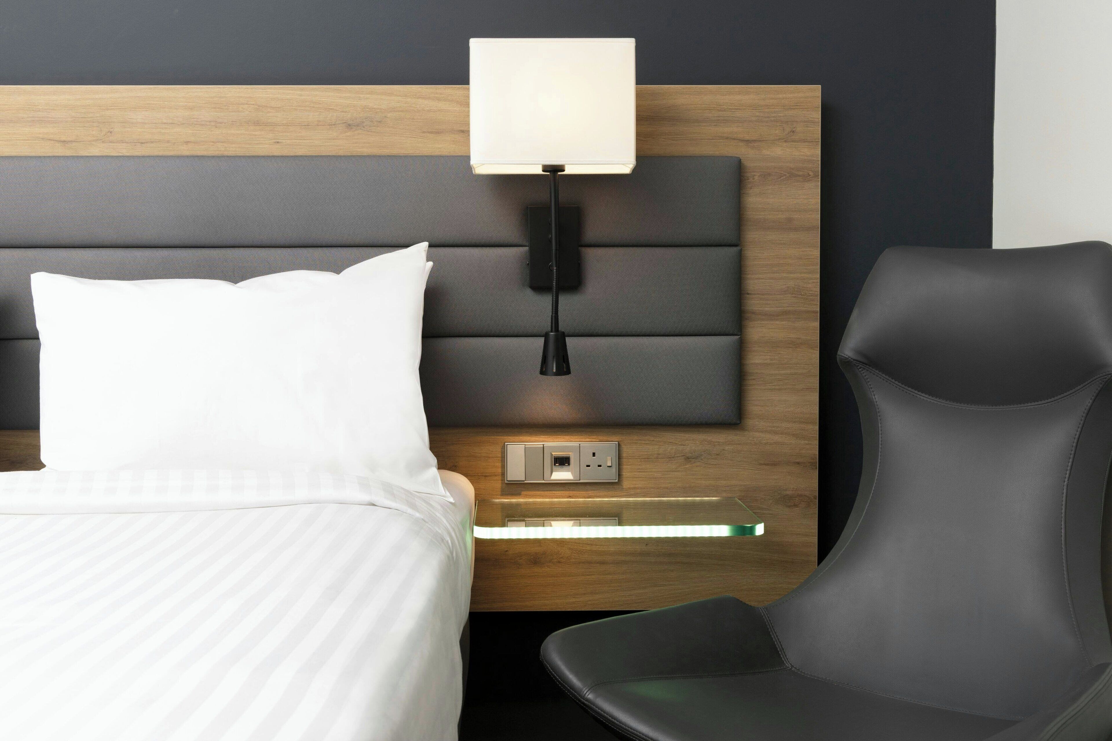 A hotel room with a bed, a nightstand, a lamp, and a chair.