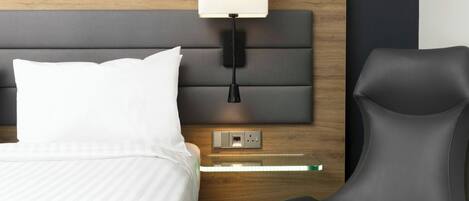A hotel room with a bed, a nightstand, a lamp, and a chair.