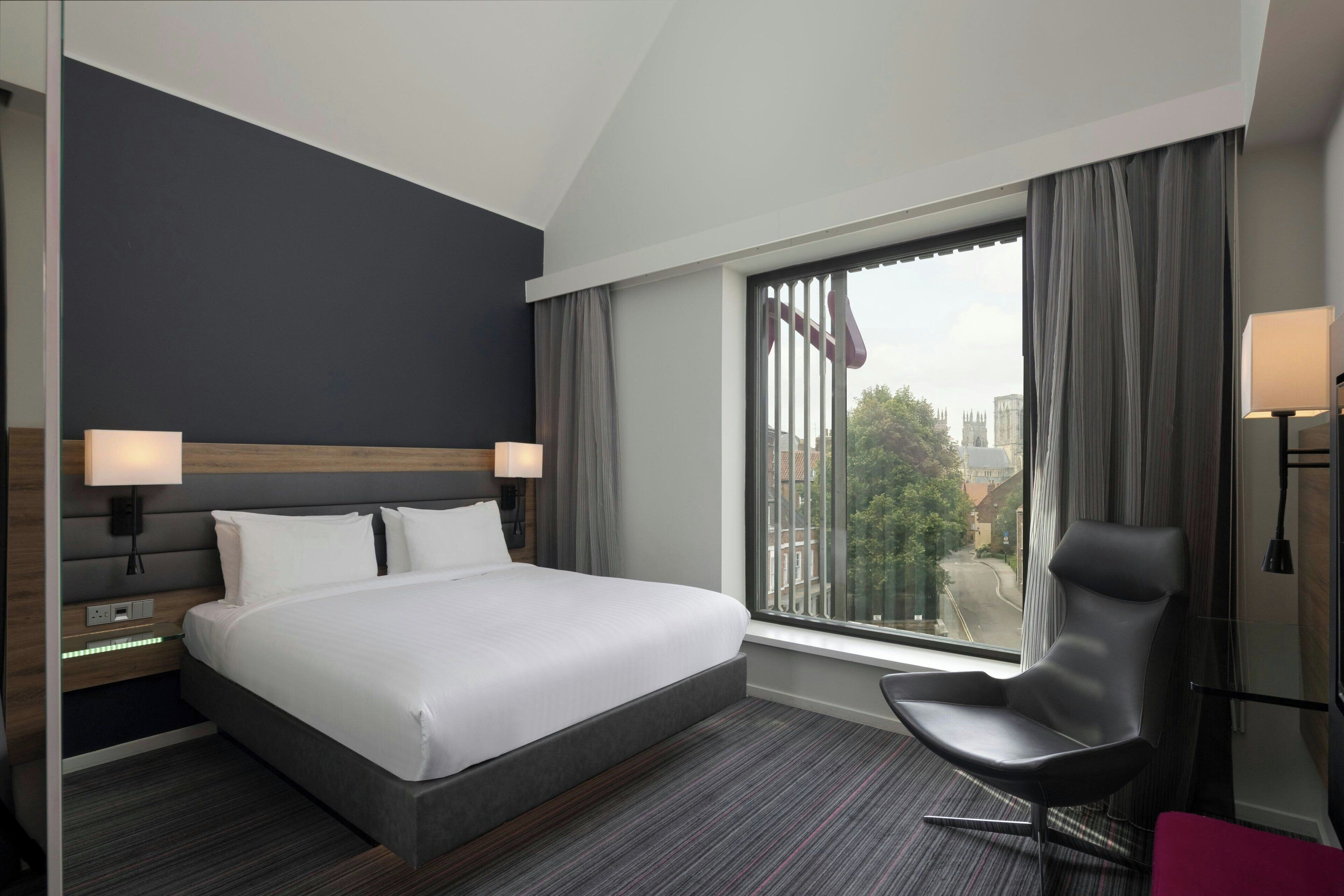 Una habitación de hotel moderna con una cama grande, una silla y una ventana con vistas a la ciudad.