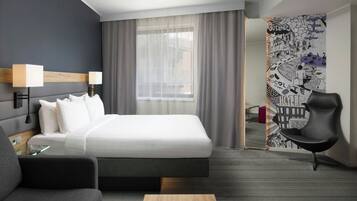 Habitació d'hotel moderna amb un llit gran, escriptori, cadira i una finestra ampla amb cortines.