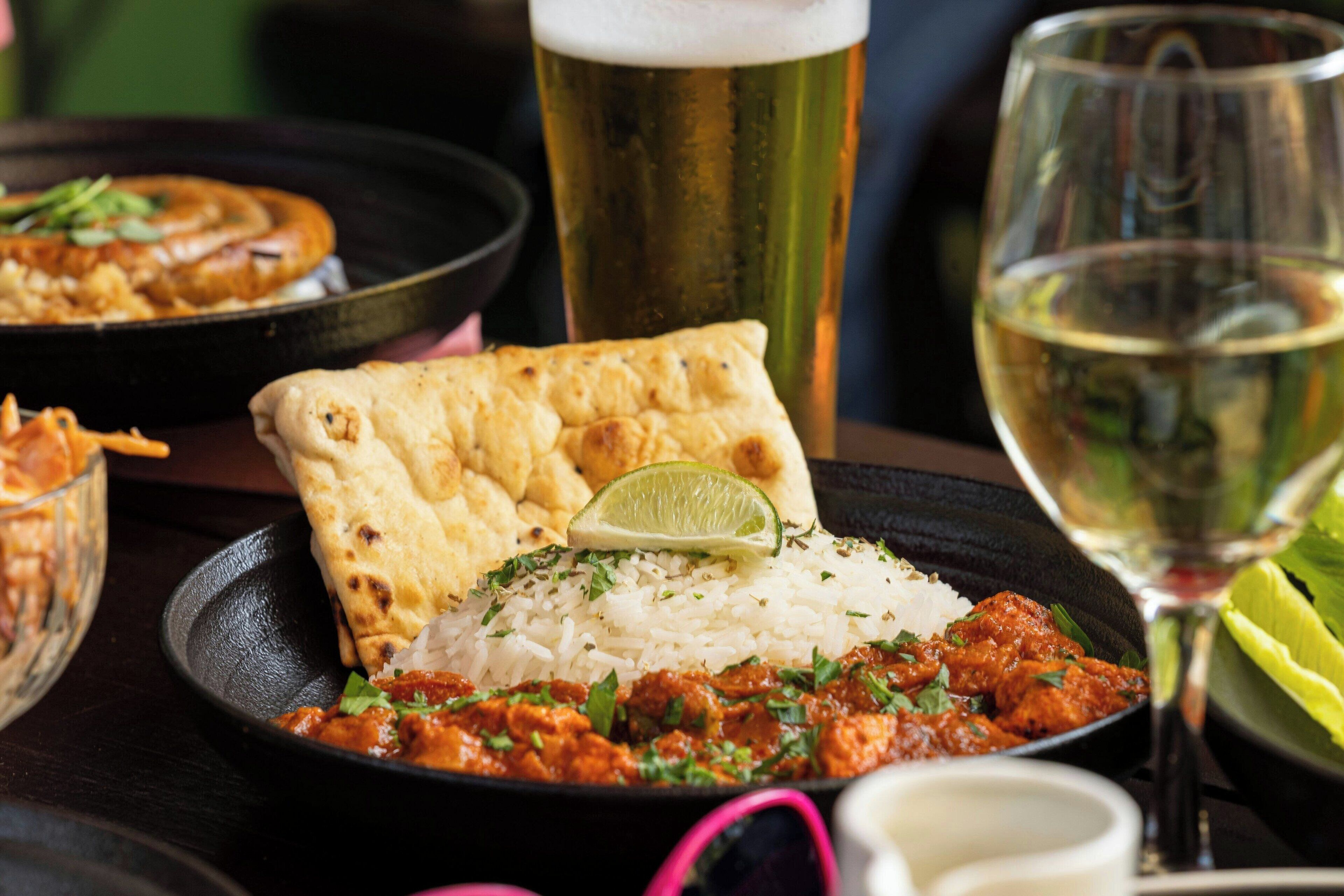 Une table dressée avec un repas composé de riz, de curry, de pain naan et d’un quartier de citron vert.