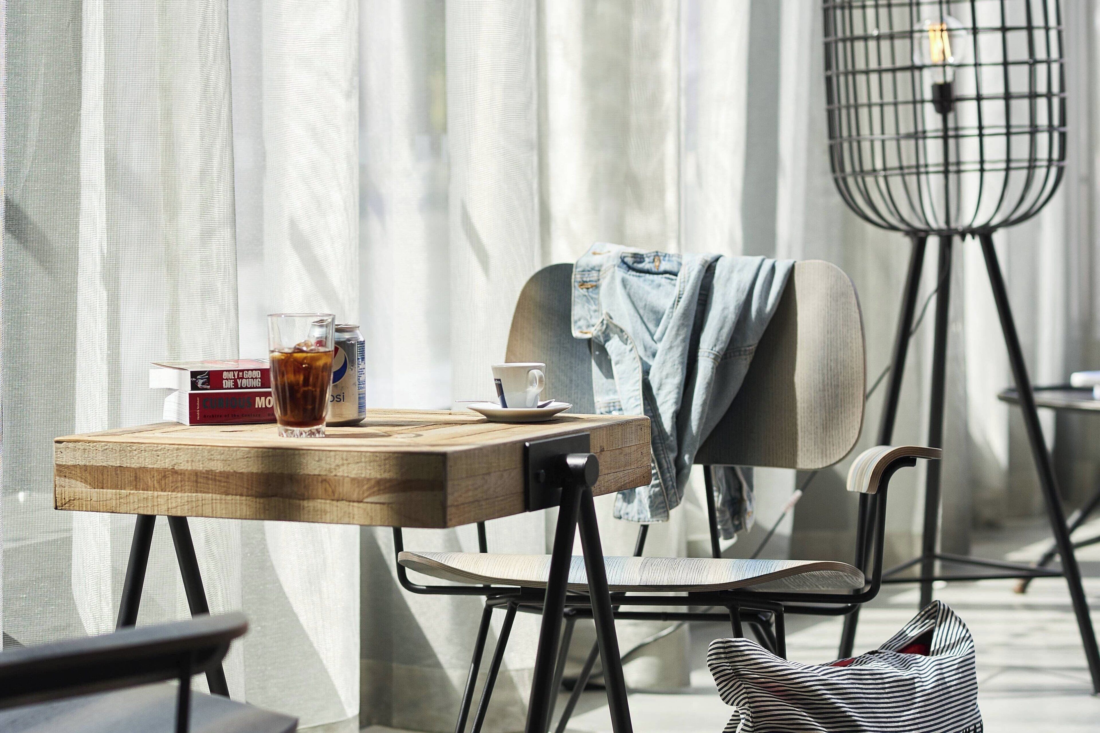 A wooden table with a glass of iced tea, a book, and a cup. A chair with a denim jacket draped over it is next to the table.
