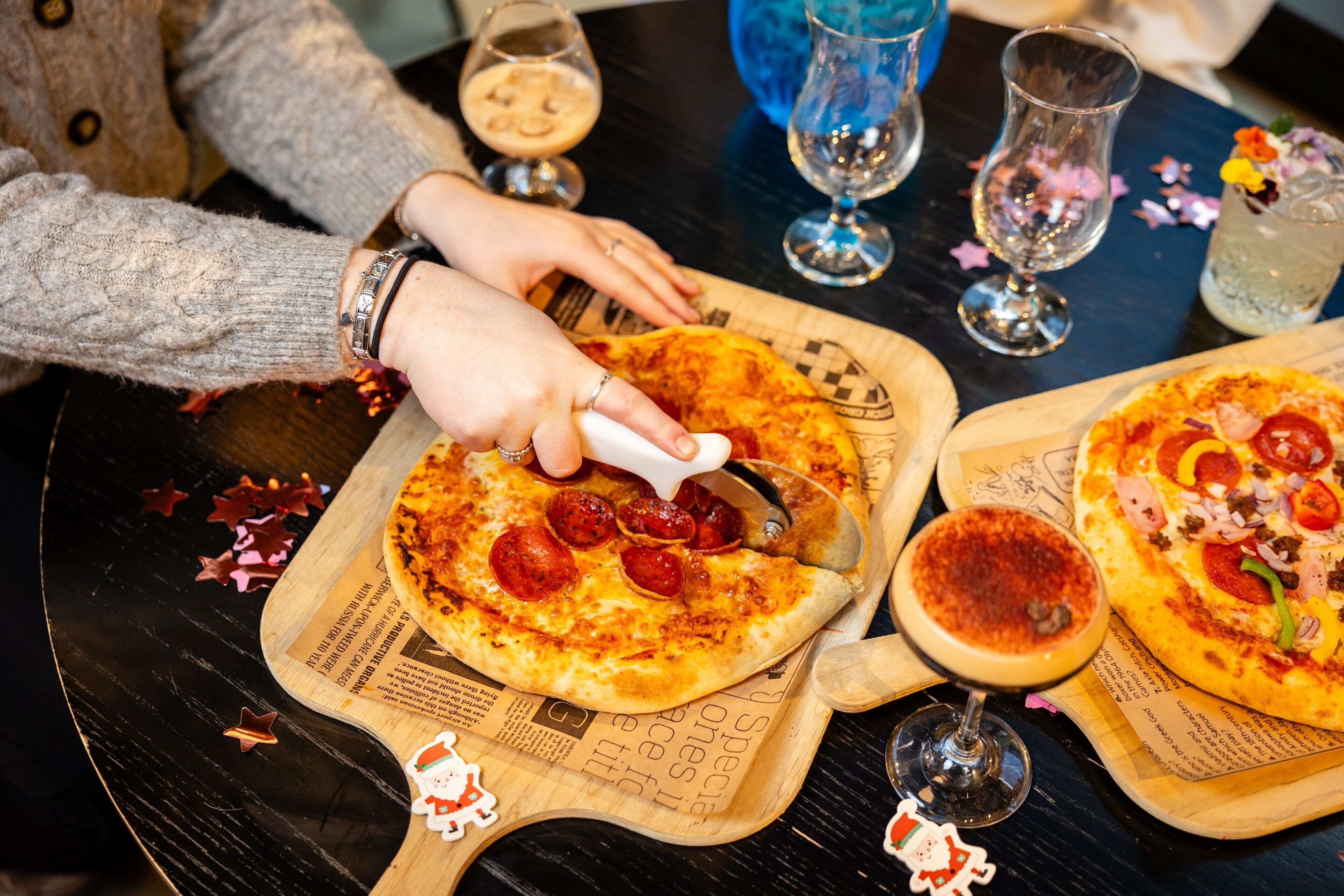 A person cutting a pizza on a wooden board with a pizza cutter.