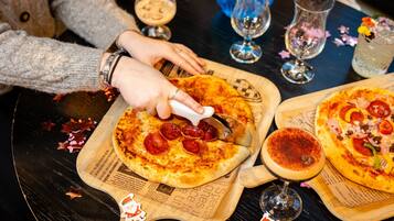 A person cutting a pizza on a wooden board with a pizza cutter.