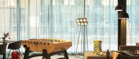 A modern living room with a foosball table, a sofa, a coffee table, and a chess set.