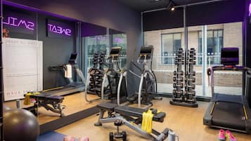 Un gimnasio con equipo de ejercicio, una cinta de correr y un espejo que refleja la sala.