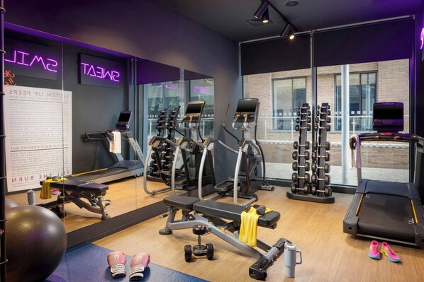 Un gimnasio con equipo de ejercicio, una cinta de correr y un espejo que refleja la sala.