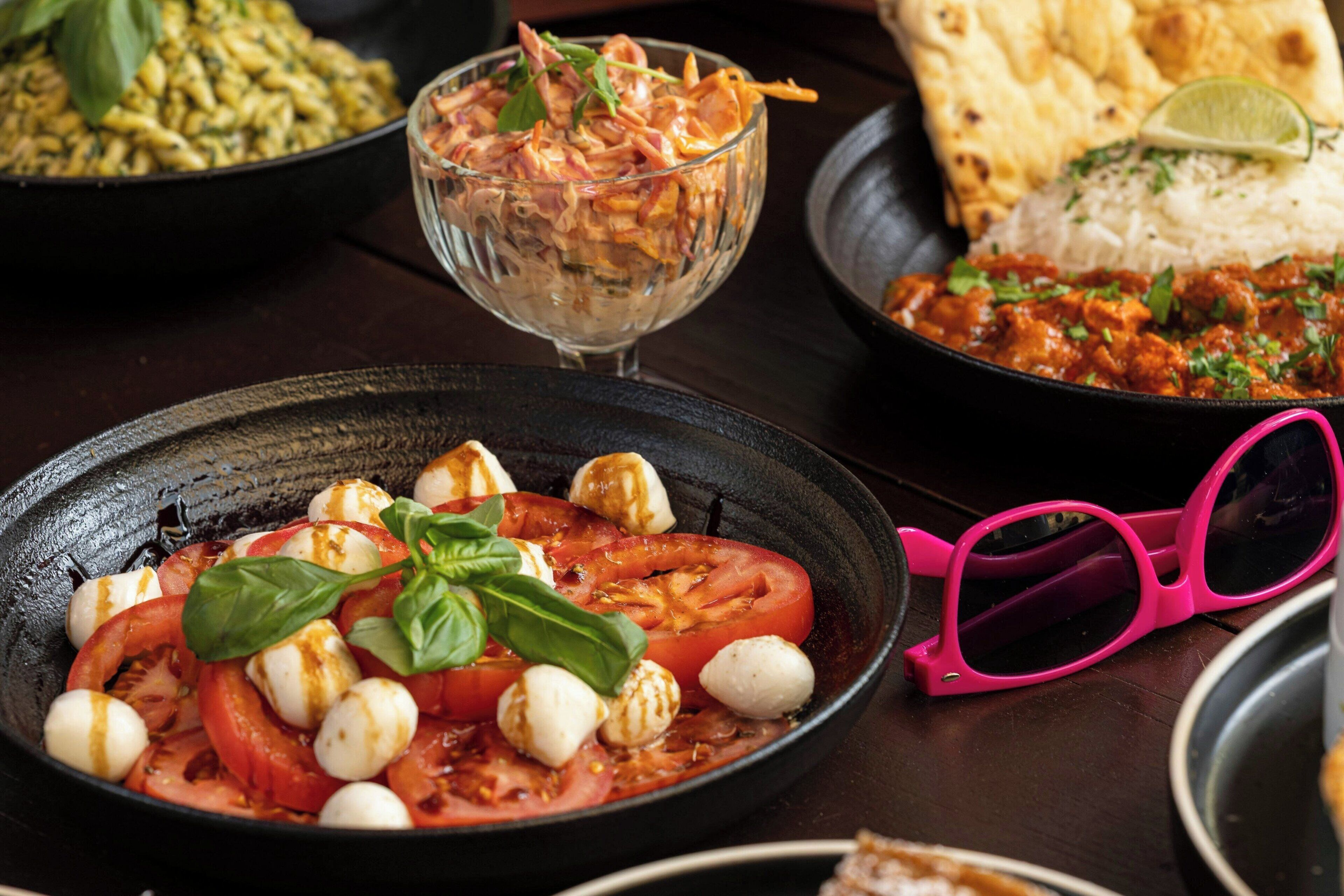 A variety of dishes including a tomato and mozzarella salad, a bowl of salad with greens and nuts, and a plate of rice with curry.